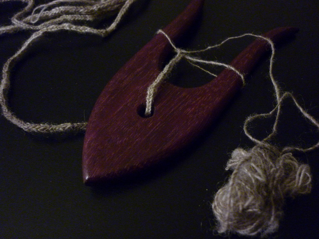 a purpleheart lucet with cord coming out one side and a ball of handspun laceweight wool on the other