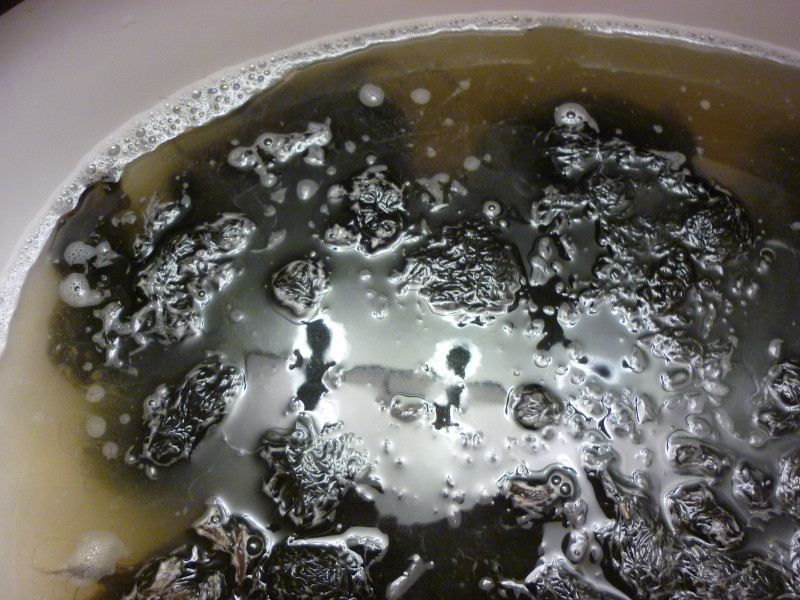 a white sink containing brown water with bubbles and piles of black wool