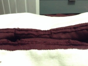 view of the inside of the waist, where single and triple box pleats are whip stitched to the bodice. Burgundy wool with dark red silk stitches.