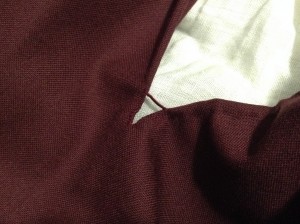 burgundy fabric on a white background revealing two hemmed edges reinforced with a buttonhole bar of dark red silk