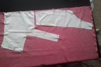 Two pieces of white fabric, shaped for a bodice, are pinned onto pink linen, waiting to be cut