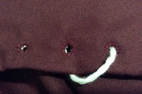 burgundy fabric with three hand sewn eyelets visible and a white fingerloop braid through one of them